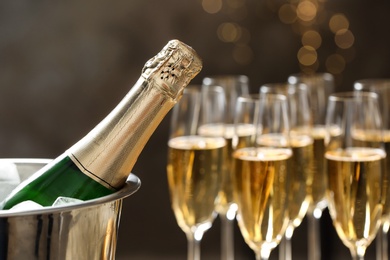 Photo of Bottle of champagne in bucket with ice and glasses on blurred background, closeup. Space for text