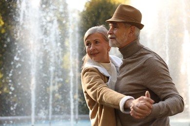 Photo of Affectionate senior couple dancing together near fountain outdoors, space for text