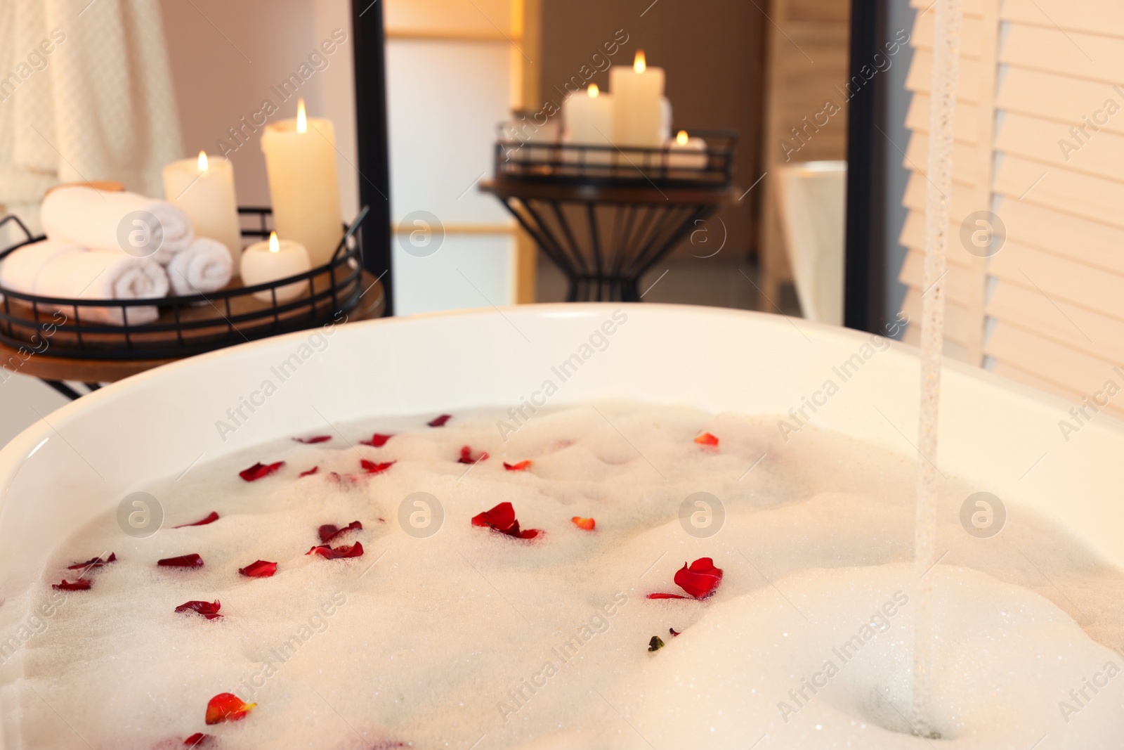 Photo of Bath tub with foam and rose petals in bathroom