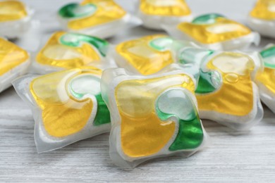 Photo of Many dishwasher detergent pods on white wooden table, closeup
