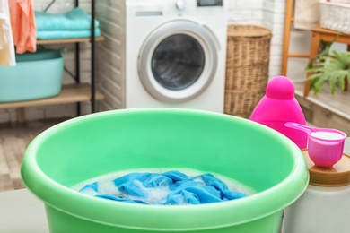 Photo of Color clothes with foam in basin and detergents on table in bathroom