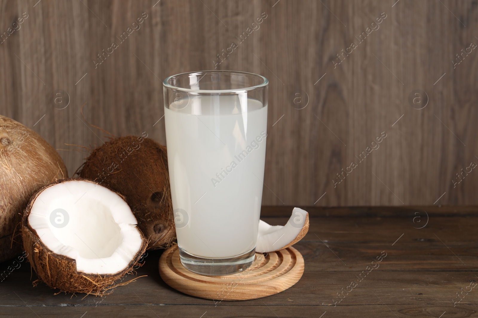 Photo of Glass of coconut water and nuts on wooden table, space for text