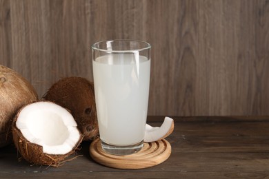 Photo of Glass of coconut water and nuts on wooden table, space for text