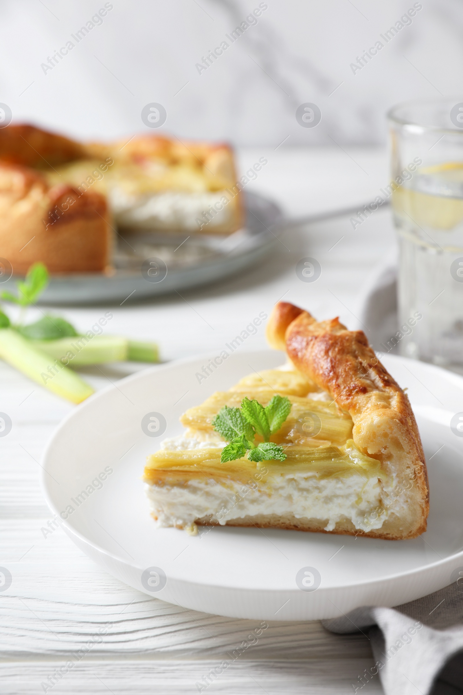 Photo of Freshly baked rhubarb pie with cream cheese, stalks and mint leaves on white wooden table, closeup