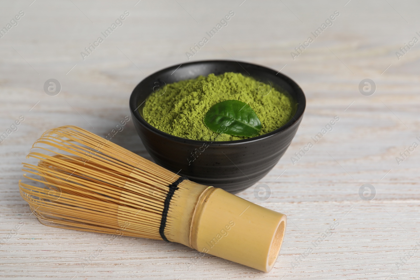 Photo of Green matcha powder and bamboo whisk on white wooden table, closeup