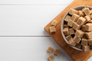 Photo of Brown sugar cubes on white wooden table, flat lay. Space for text