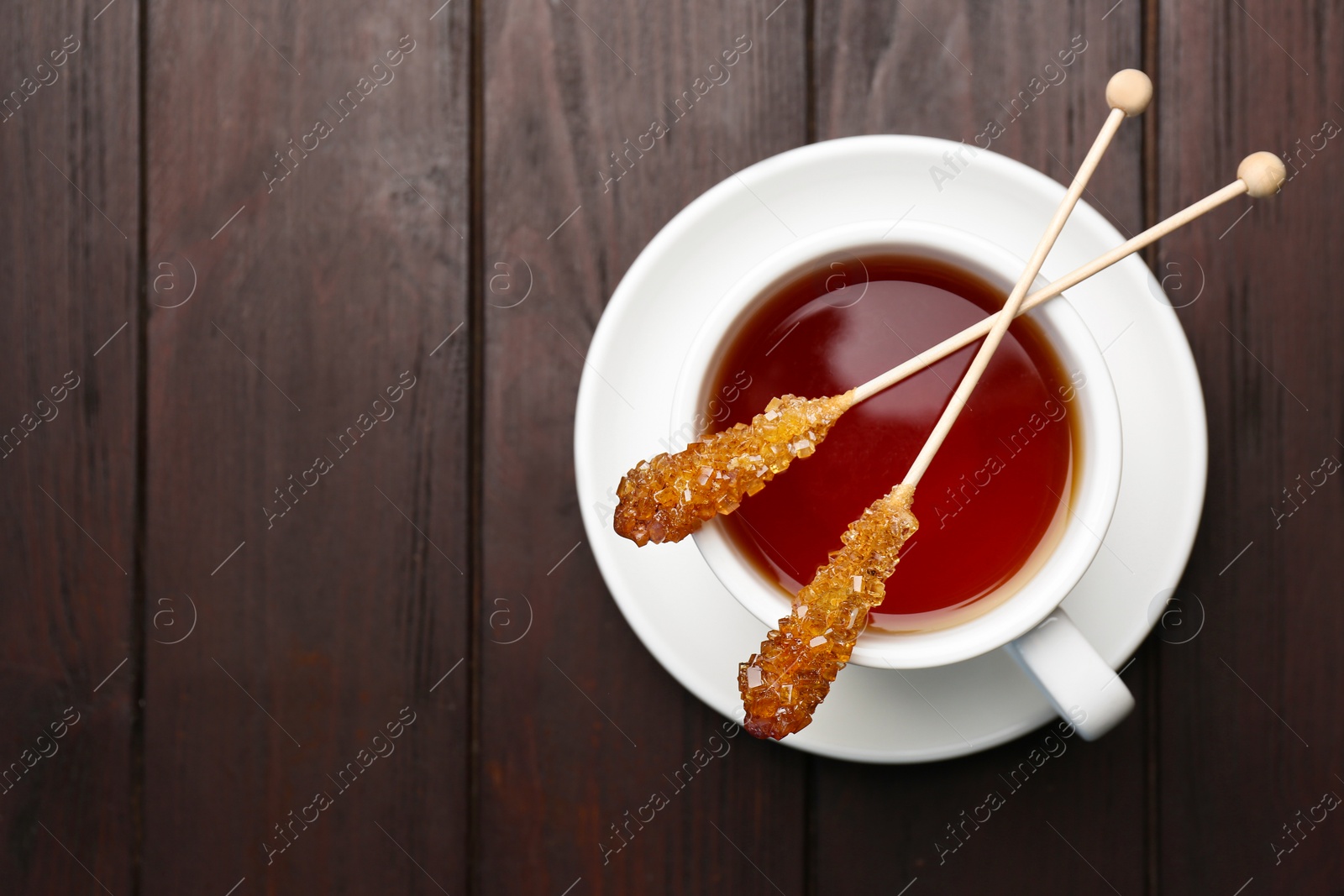 Photo of Sticks with sugar crystals and cup of tea on wooden table, top view. Space for text