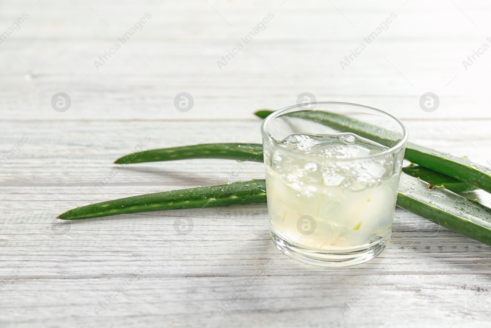 Photo of Glass with aloe vera gel and green leaves on wooden table. Space for text