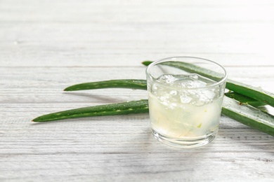 Glass with aloe vera gel and green leaves on wooden table. Space for text