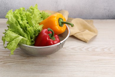 Photo of Colander with fresh lettuce and bell peppers on wooden table, space for text