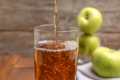 Photo of Pouring fresh apple juice into glass on wooden background, closeup