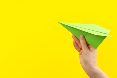 Woman holding paper plane on yellow background, closeup. Space for text