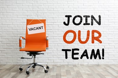 Image of Join our team! Orange office chair with sign VACANT near white brick wall indoors