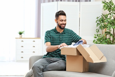 Photo of Young man opening parcel on sofa at home