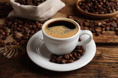 Cup of aromatic hot coffee and beans on wooden table