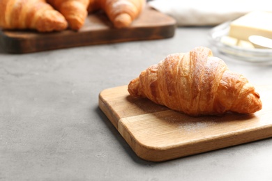 Photo of Wooden board with tasty croissant and space for text on grey table. French pastry