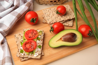 Photo of Fresh crunchy crispbreads with cream cheese, tomatoes and avocado on beige table