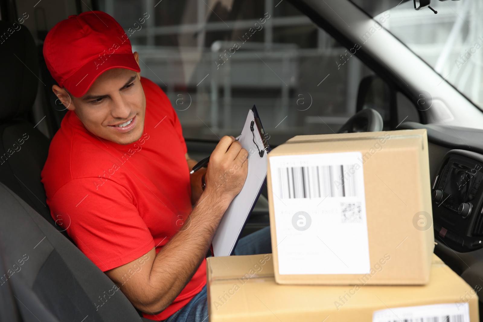 Photo of Courier with clipboard checking packages in car