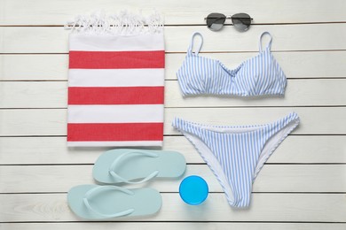 Photo of Beach towel, swimsuit, flip flops and sunglasses on white wooden background, flat lay