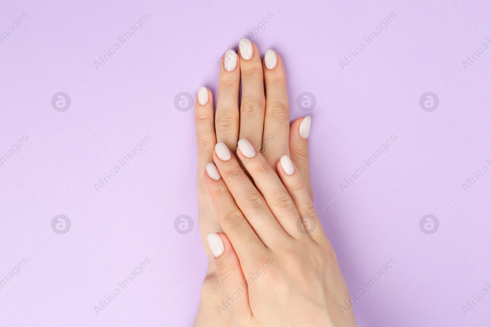 Photo of Woman with white polish on nails against violet background, top view