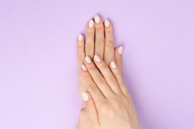 Woman with white polish on nails against violet background, top view
