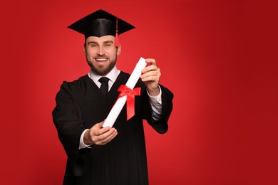 Photo of Happy student with graduation hat and diploma on red background. Space for text