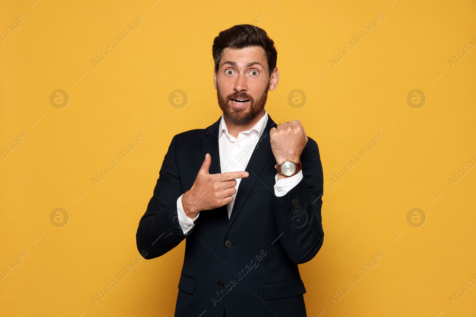 Photo of Emotional man showing time on watch against orange background. Being late concept