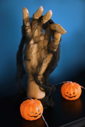 Photo of Jack-o'-lantern lights and wooden hand on black fireplace table near blue wall