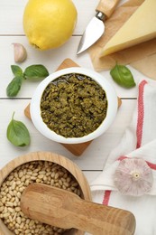 Photo of Delicious pesto sauce in bowl and ingredients on white wooden table, flat lay