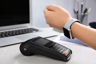 Photo of Woman using terminal for contactless payment with smart watch at table