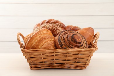 Wicker basket with different tasty freshly baked pastries on white table