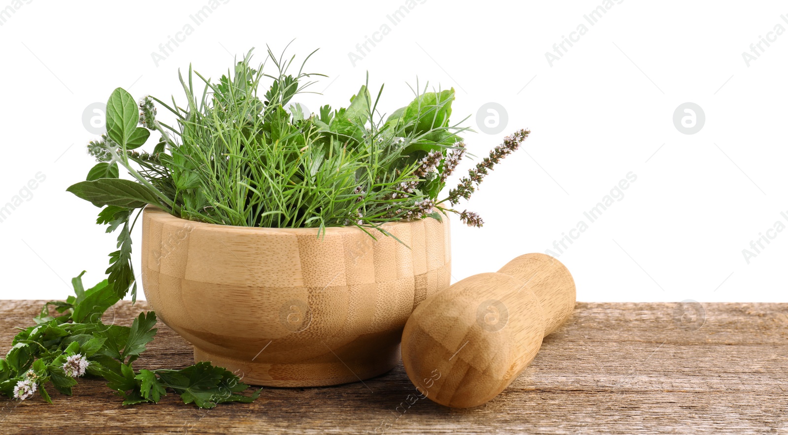 Photo of Mortar, pestle and different herbs on wooden table against white background