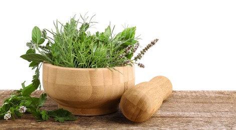 Mortar, pestle and different herbs on wooden table against white background