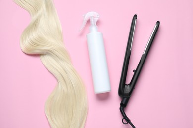Photo of Spray bottle with thermal protection, iron and lockblonde hair on pink background, flat lay