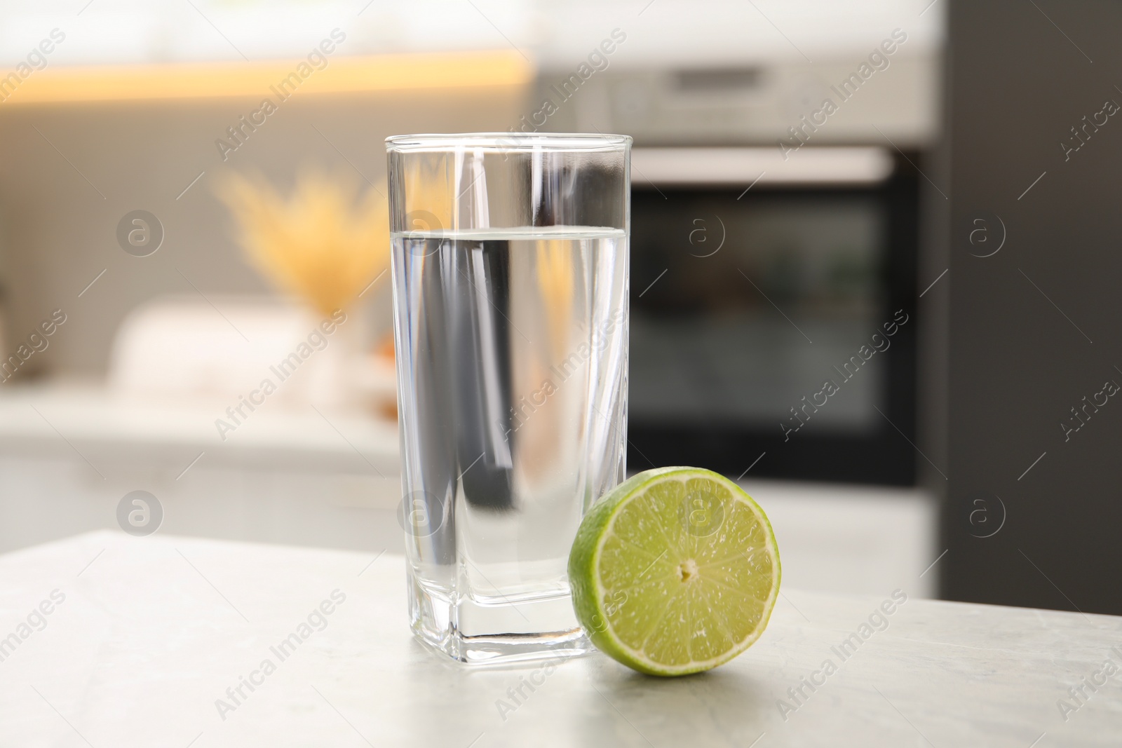 Photo of Filtered water in glass and lime on light table in kitchen, closeup