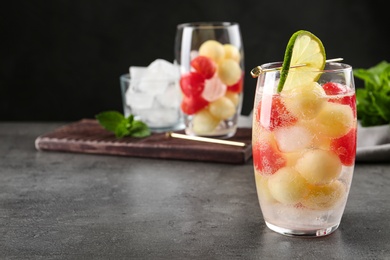 Photo of Glass of melon and watermelon ball cocktail with lime on grey table. Space for text