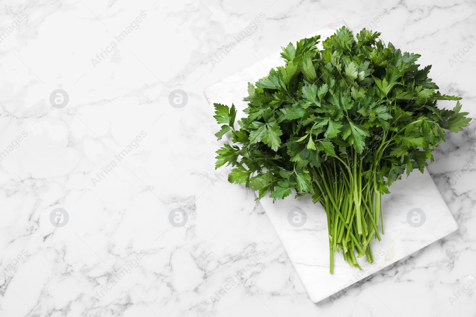 Photo of Bunch of fresh green parsley on white marble table, top view. Space for text