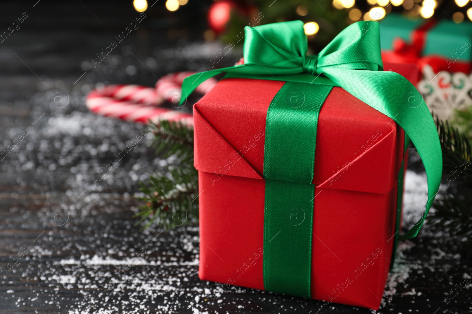 Photo of Christmas gift box with green bow on black wooden table, closeup. Space for text