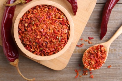 Aromatic spice. Red chili pepper flakes in bowl, spoon and pods on wooden table, flat lay