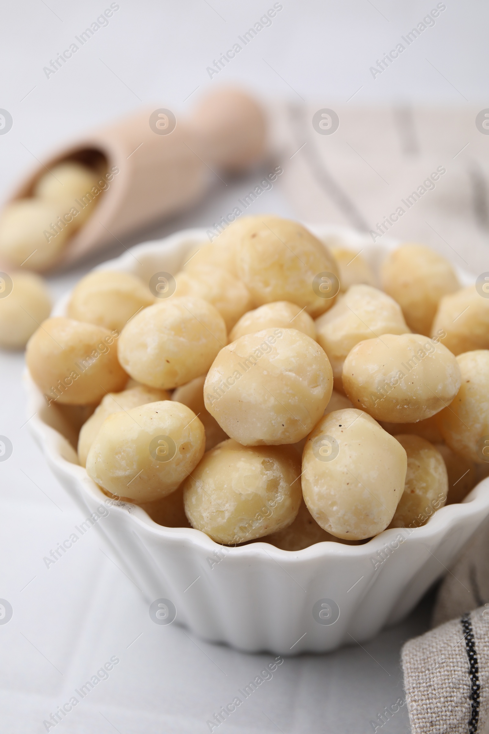 Photo of Tasty peeled Macadamia nuts in bowl on white table, closeup