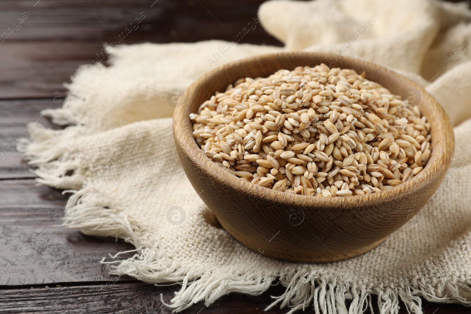 Photo of Dry pearl barley in bowl on wooden table, closeup