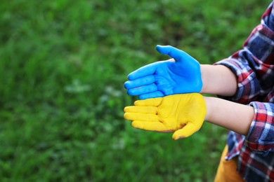 Photo of Little boy with hands painted in Ukrainian flag colors outdoors, closeup and space for text. Love Ukraine concept