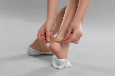 Photo of Girl putting sticking plaster onto foot on light grey background, closeup