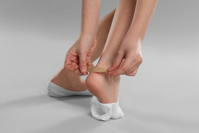 Girl putting sticking plaster onto foot on light grey background, closeup