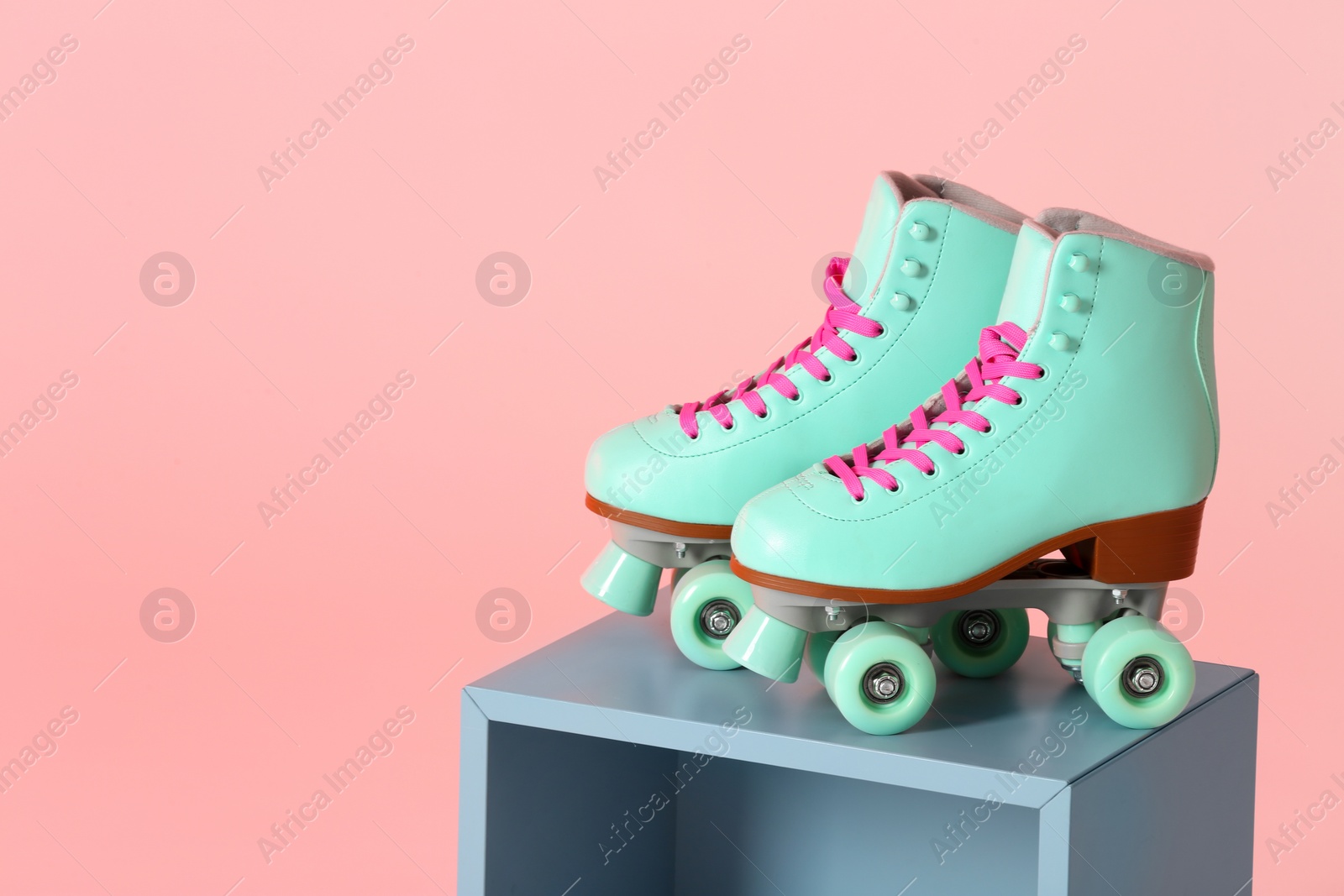 Photo of Pair of vintage roller skates on storage cube against color background. Space for text