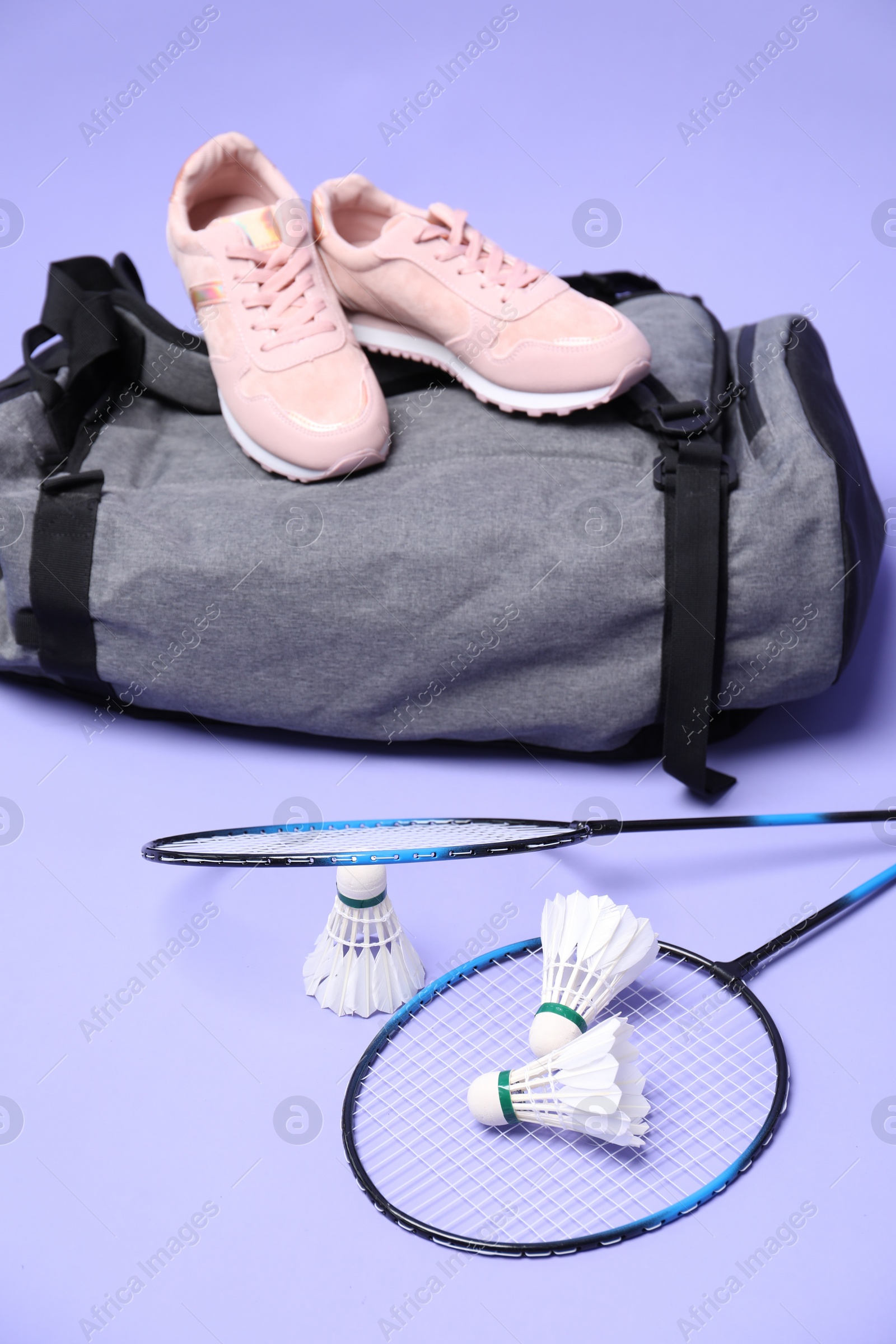Photo of Feather badminton shuttlecocks, rackets, bag and sneakers on violet background
