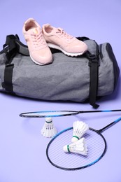 Feather badminton shuttlecocks, rackets, bag and sneakers on violet background