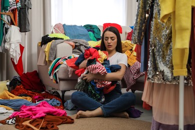 Photo of Upset young woman with lots of clothes in room. Fast fashion