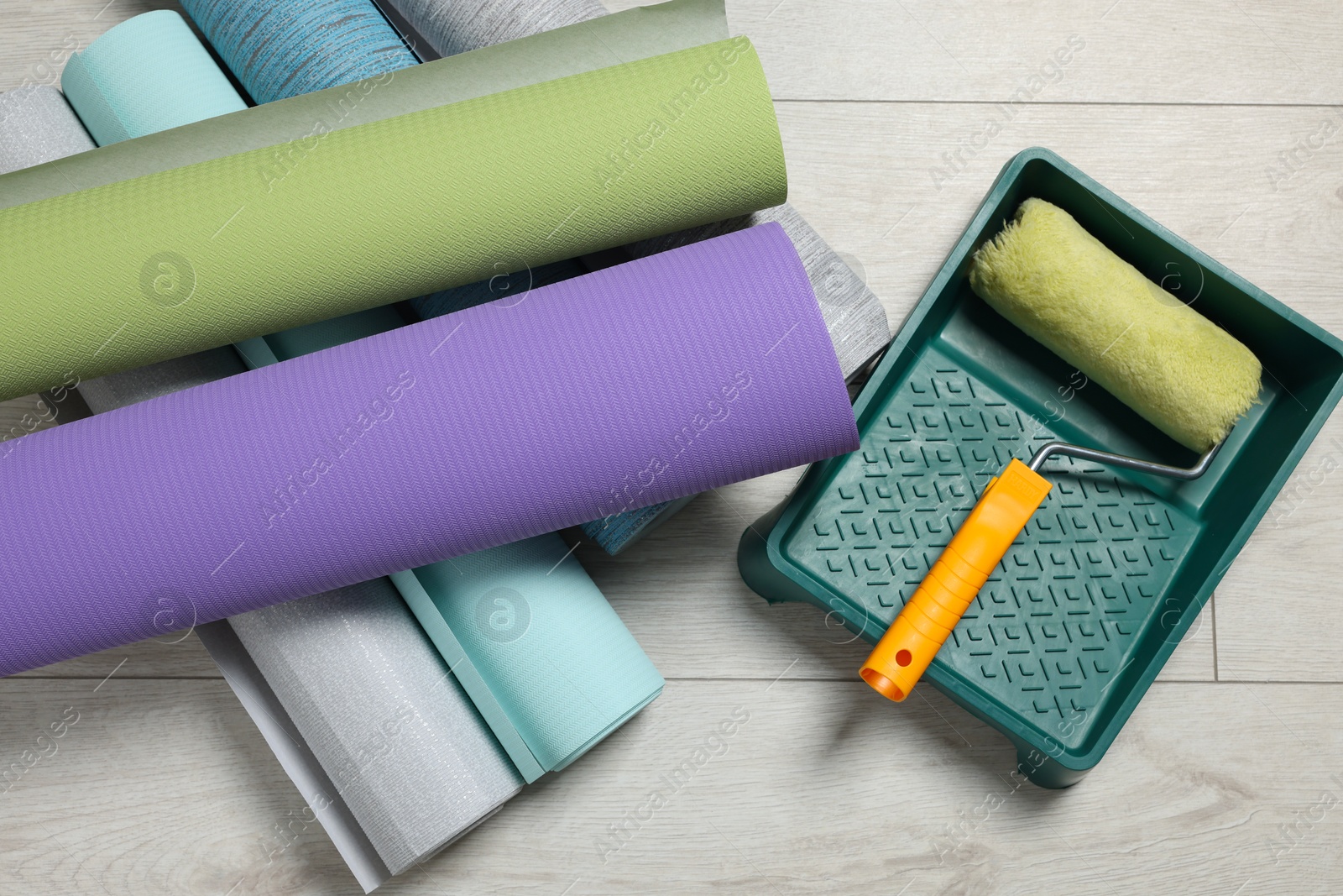 Photo of Different wallpaper rolls, roller and tray on floor, top view