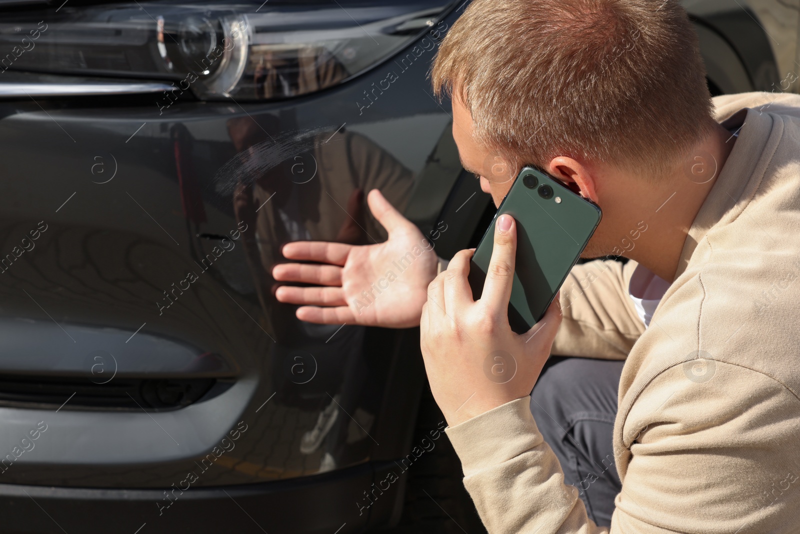 Photo of Man talking on phone near car with scratch outdoors